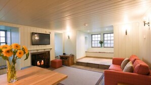 A cozy living room with a wooden ceiling, a fireplace, a TV mounted on the wall, and a red sofa.