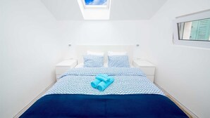 A bedroom with a skylight, a bed with patterned bedding, two bedside tables, and a window with shutters. - Penthouse apartment Sea (Bol)