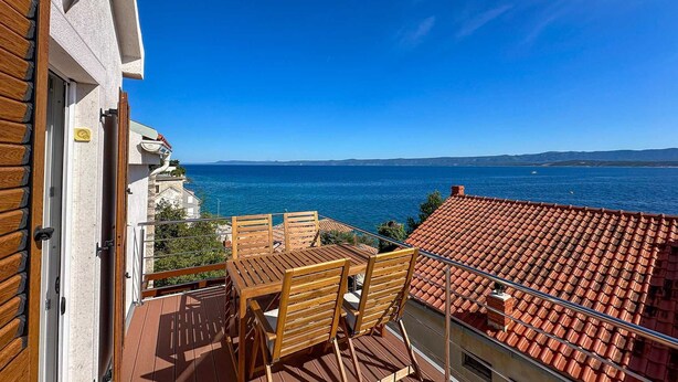 A balcony with a wooden table and chairs, overlooking a sea with a clear sky. - Penthouse apartment Sea (Bol)
