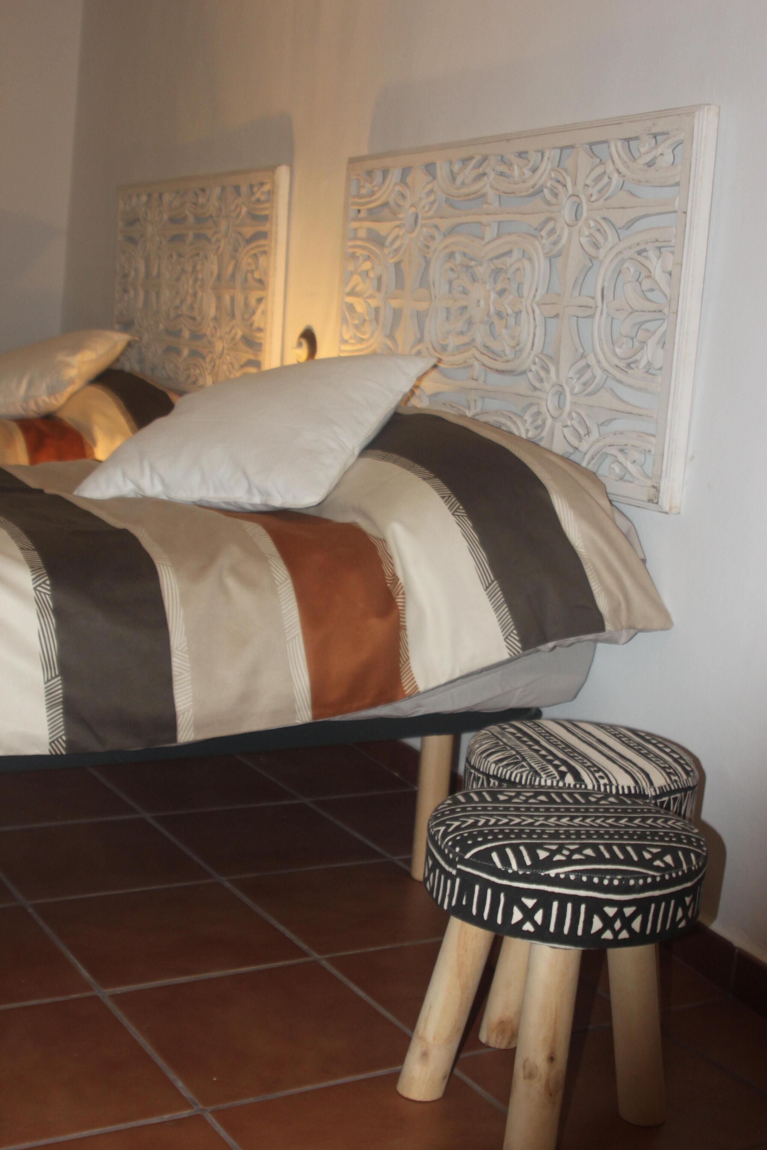 Un lit avec une couverture à rayures et des oreillers, un tabouret en bois et des panneaux décoratifs sur les murs.
