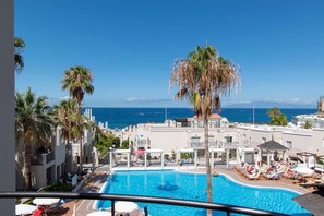 A hotel pool area with a view of the ocean, palm trees, and a clear blue sky.