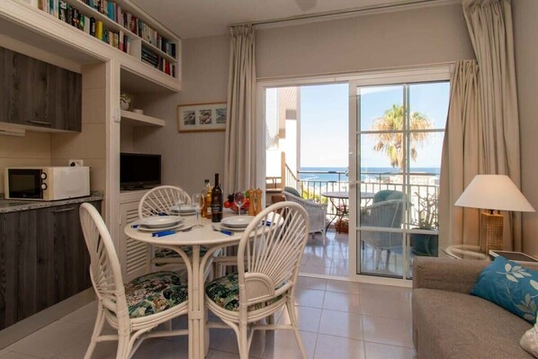A dining area with a table and chairs, a kitchen area with a microwave, and a view of the ocean through a sliding glass door.