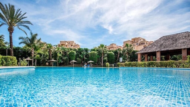 Una piscina con agua azul cristalina, rodeada de palmeras y edificios de techos planos.