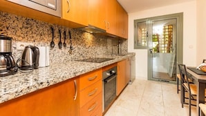 Una cocina con encimeras de granito, gabinetes de madera, electrodomésticos de acero inoxidable y un vidrio que da a un balcón.