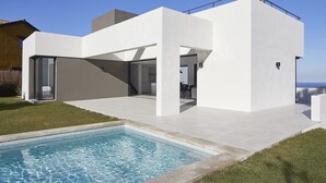 Ein modernes Haus mit Swimmingpool, großen Glasfenstern und Meerblick.