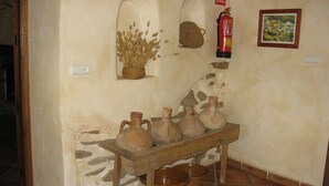 A rustic interior with a stone wall, a wooden table holding several pottery items, a fire extinguisher, and a framed picture. - Rural house (rental entire) Reul Alto Cortijos Rurales for 6 people (Laroya)
