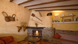 A cozy room with a stone fireplace, a wooden shelf with books, and a woven basket. - Rural house (rental entire) Reul Alto Cortijos Rurales for 6 people (Laroya)