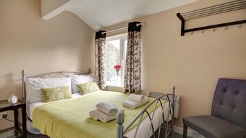 A neatly arranged bedroom with a bed, a chair, a bedside table with a clock, and a window with curtains.