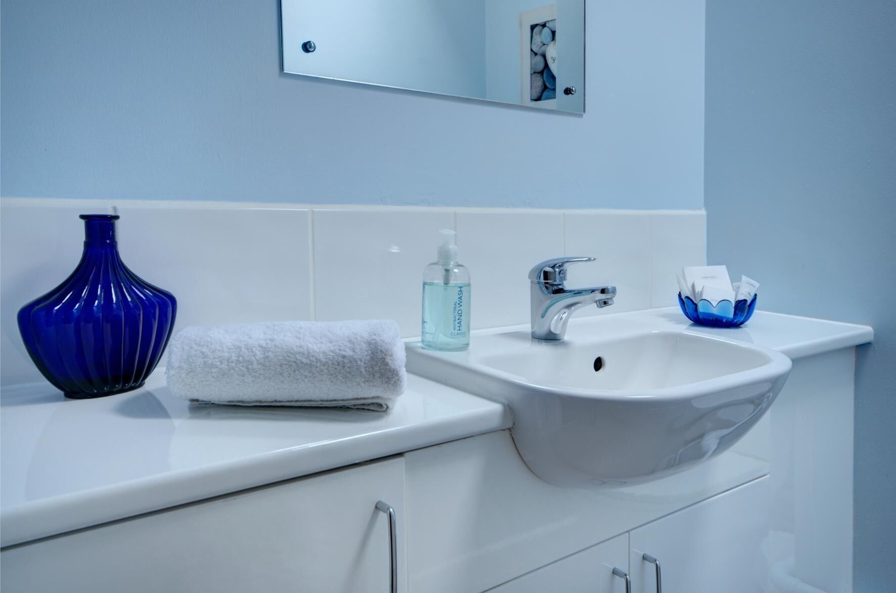 Een badkamer met een witte wastafel, een blauwe vaas, een witte handdoek, een zeepdispenser en een blauwe zeepbakje.