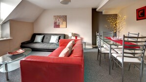 Una sala moderna con un sofá rojo, un sofá gris y un comedor con una mesa de vidrio y sillas de metal.