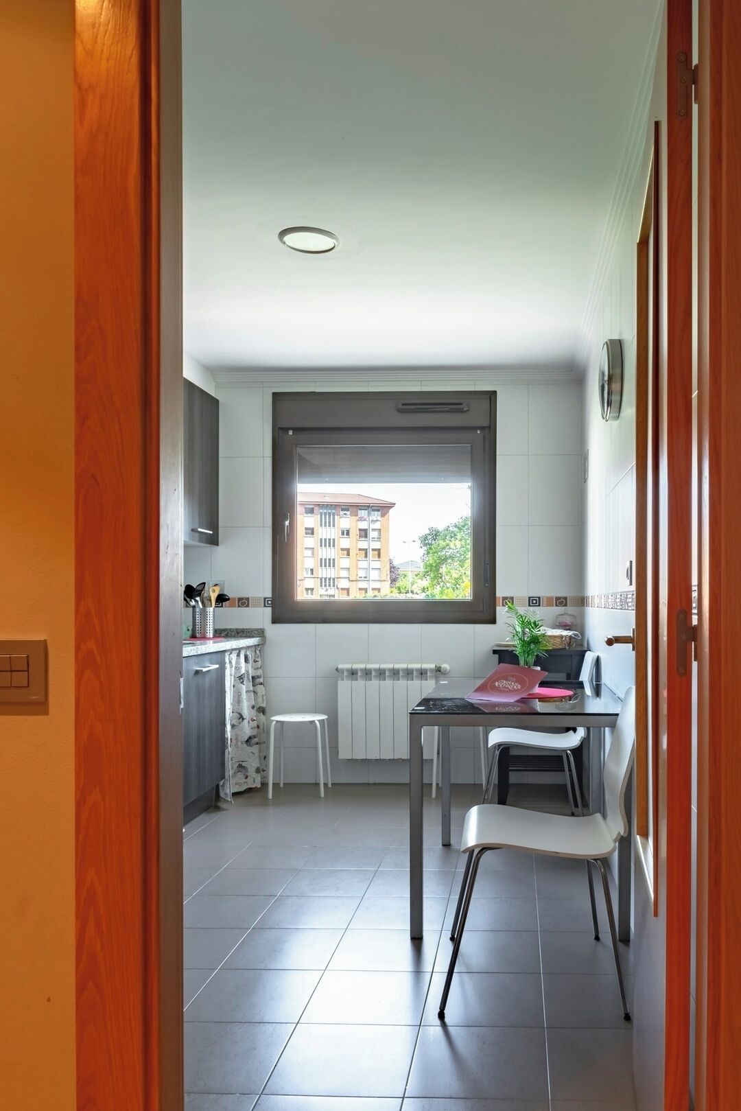 A modern kitchen with a window, a dining area with a table and chairs, and a view of a building outside.