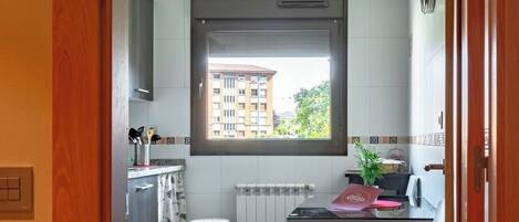 A modern kitchen with a window, a dining area with a table and chairs, and a view of a building outside.