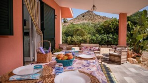 An outdoor dining area with a table set for two, wicker furniture, and a view of a mountain.