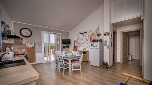 A modern kitchen with a dining area, wooden flooring, and a TV mounted on the wall.