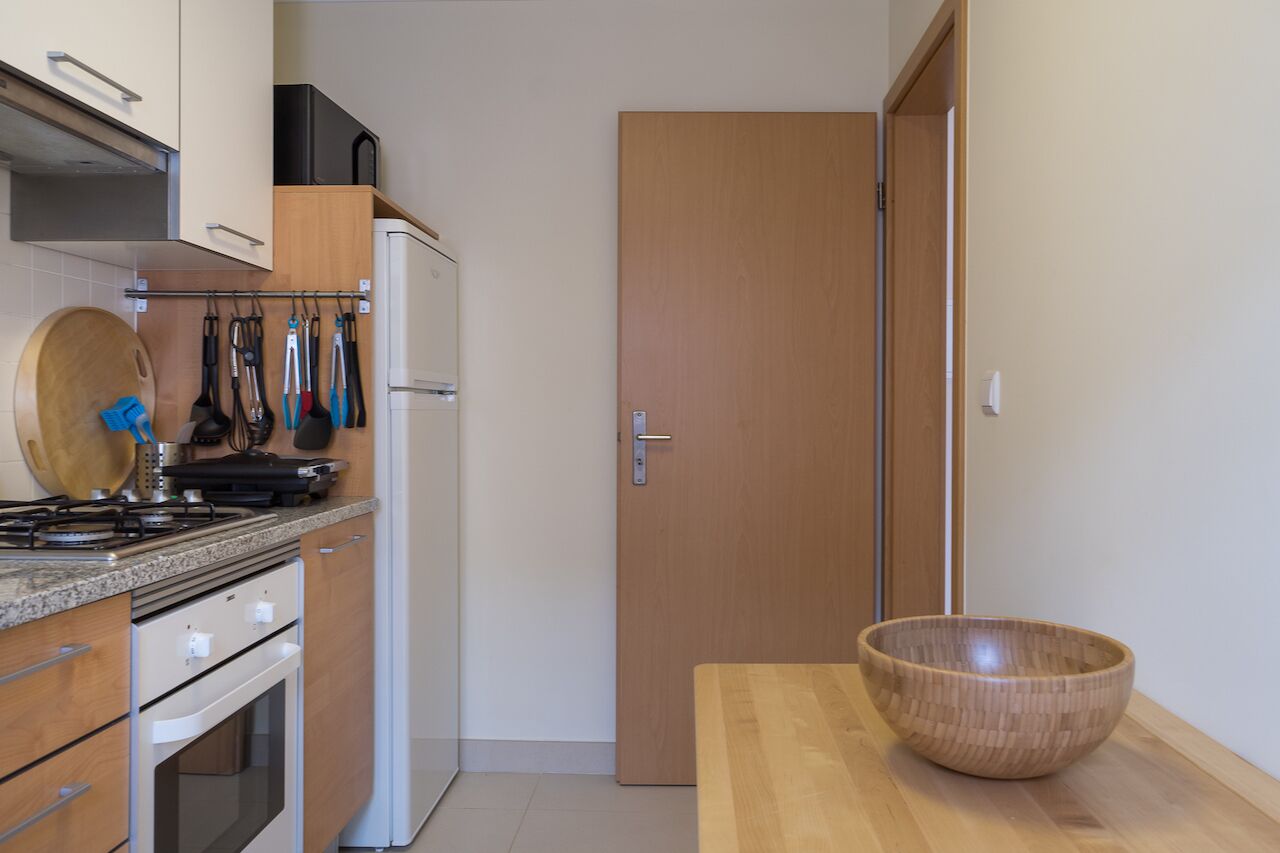 A compact kitchen with a stove, oven, and refrigerator. There is a wooden bowl on the counter and a door to the right.
