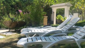 Ein Garten mit weißen Liegestühlen, einer Pergola und Kübelpflanzen.