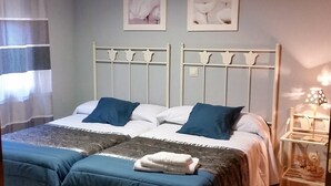 Ein ordentlich bezogenes Bett mit blauer und weißer Bettwäsche, ein Nachttisch mit einer Lampe und zwei gerahmte Bilder an der Wand.