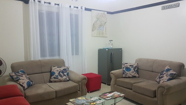 Una sala de estar con dos sofás color beige, una mesa de centro de vidrio, un reposapiés rojo, un refrigerador y un mapa en la pared.