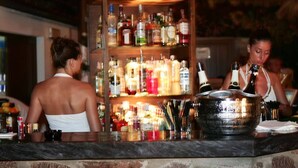 Een bar met verschillende drankflessen op planken en een grote metalen container op de toonbank.