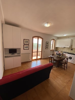 Ein kompakter Wohnbereich mit Essplatz, Küchenzeile und einem roten Sofa.