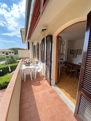 Ein Balkon mit Tisch und Stühlen, einer Blumenkomposition und Blick auf ein Gebäude im Hintergrund.