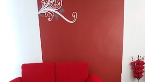 A red sofa against a white and red wall with a decorative swirl design. A wooden coffee table with a red cloth featuring sunflowers is in front.