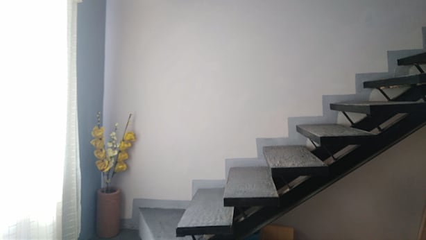 A staircase with a modern design, a potted plant with yellow flowers, and a window with curtains.