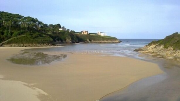 A beach with a sandy shore, a few scattered rocks, and a building on a hill in the background.