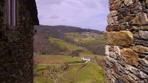 A stone building with a view of a rural landscape, including fields and a distant white house.