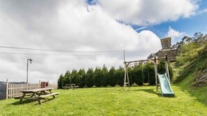 A grassy outdoor area with picnic tables, a wooden fence, and a playground with a slide.