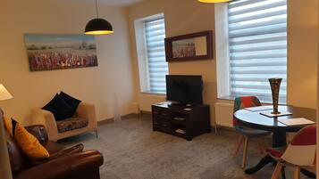 A living room with a sofa, a TV, a dining table with chairs, and artwork on the walls.