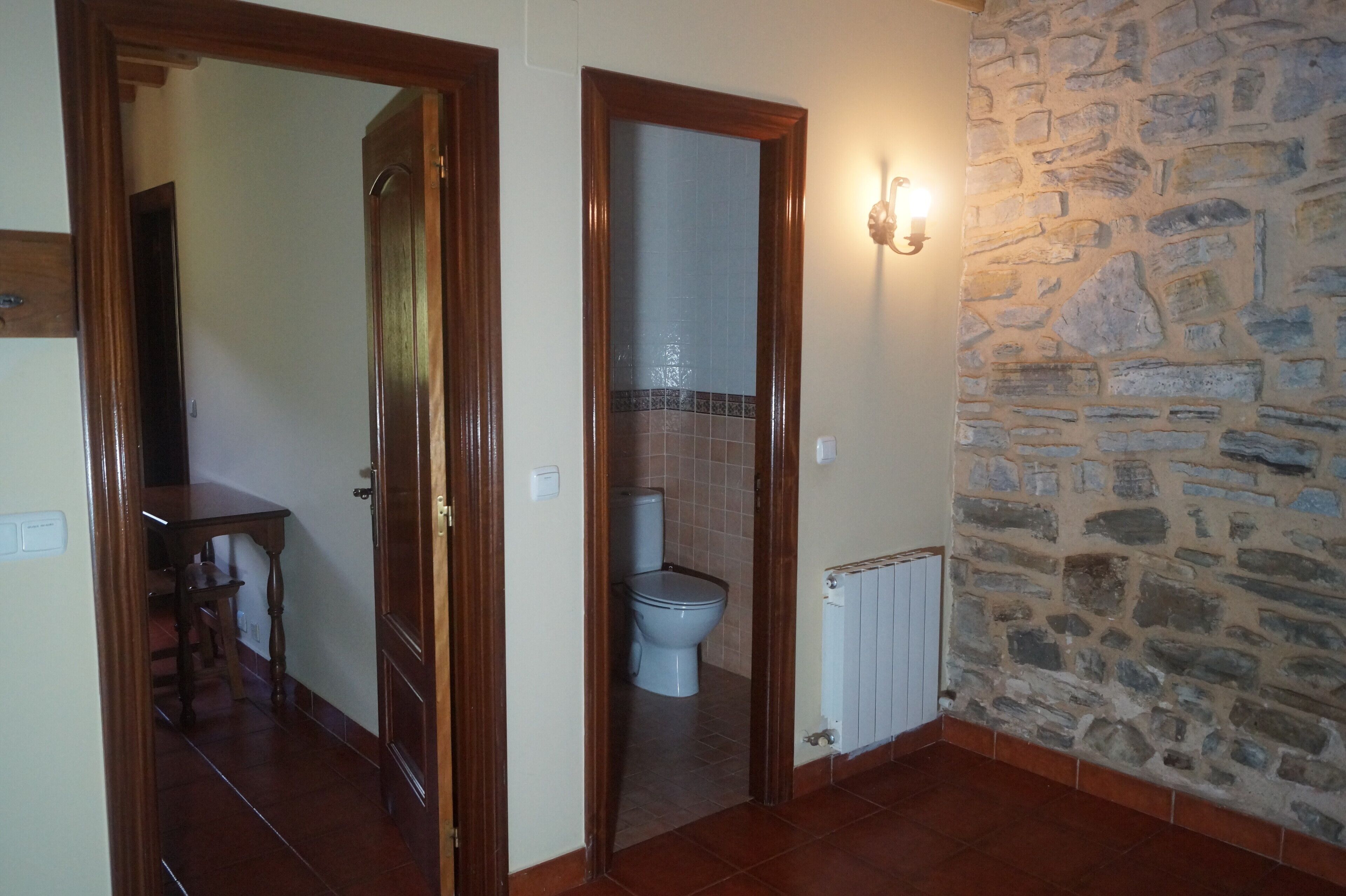 A hallway with a wooden door leading to a bathroom with a toilet and a tiled wall.