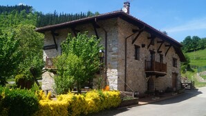 A stone building with a balcony, surrounded by greenery and a clear sky. - Goikoetxe Baserria in Zeanuri (Zeanuri)
