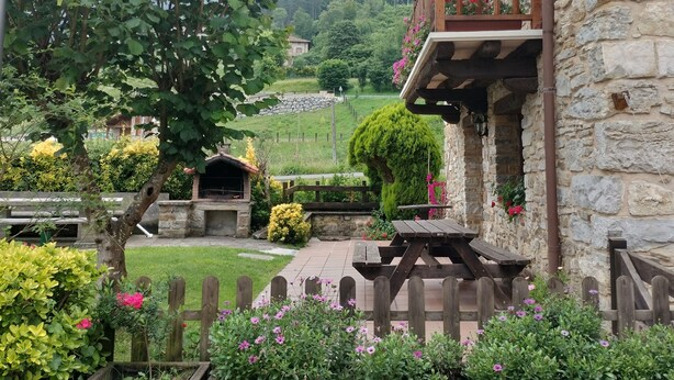 A rustic stone building with a wooden balcony, surrounded by lush greenery and a stone pathway. - Goikoetxe Baserria in Zeanuri (Zeanuri)