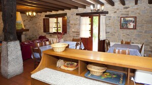A rustic dining area with stone walls, wooden beams, and a long wooden table with baskets and a fruit platter. - Goikoetxe Baserria in Zeanuri (Zeanuri)