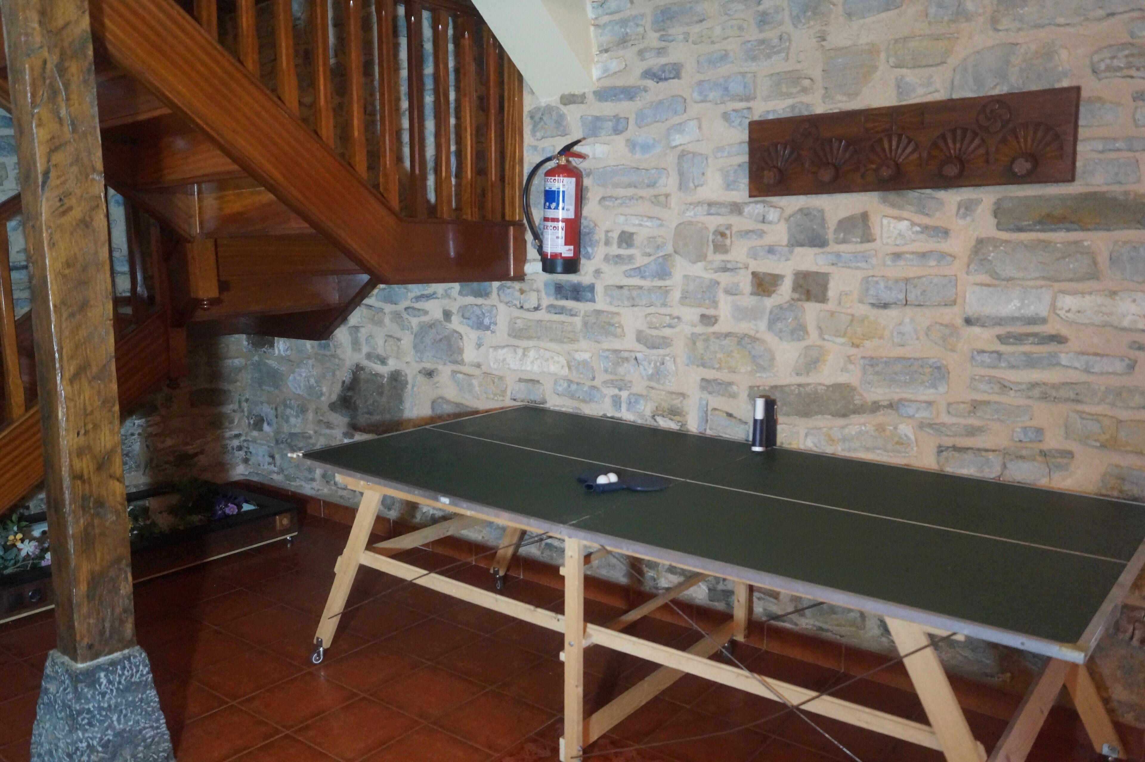 A ping pong table in a room with stone walls and a wooden staircase.