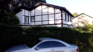 A house with a white exterior and dark trim, a car parked in front, and a hedge in the foreground. - holiday home in galdames (galdames,vizcaya)