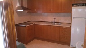 A compact kitchen with wooden cabinets, a stainless steel sink, and a white refrigerator. - holiday home in galdames (galdames,vizcaya)