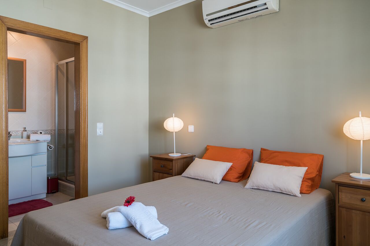 Ein ordentlich eingerichtetes Hotelzimmer mit einem Bett, Nachttischlampen und einem durch eine geöffnete Tür einsehbaren Badezimmer.