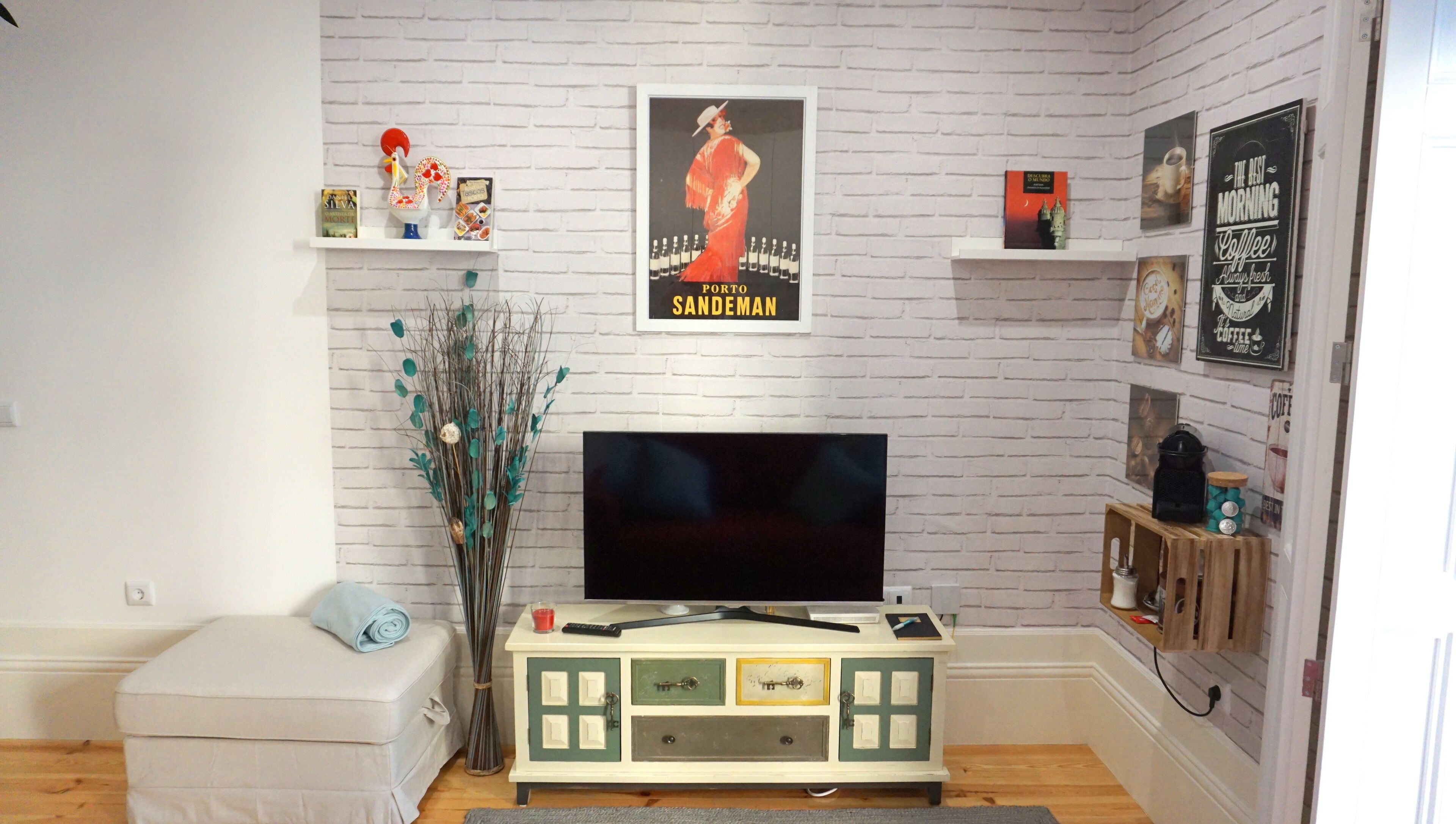 A living room with a flat-screen TV, a vintage-style cabinet, and a wall-mounted poster.