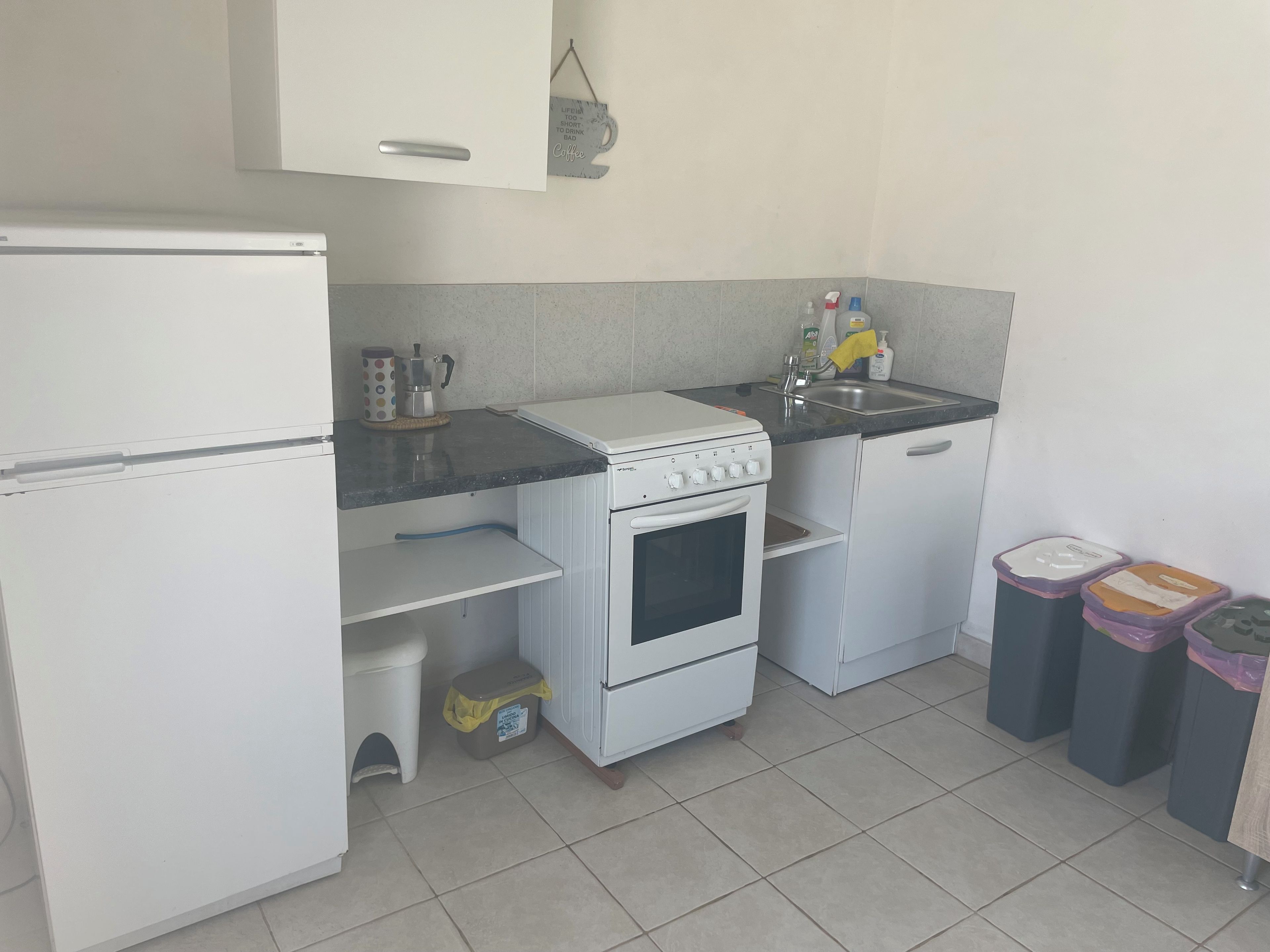 Eine kleine Küche mit Kühlschrank, Herd, Spüle und Mülleimern.