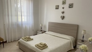 Una cama bien hecha con toallas dobladas, una mesita de noche con lámpara y una pared decorada con motivos de corazón.