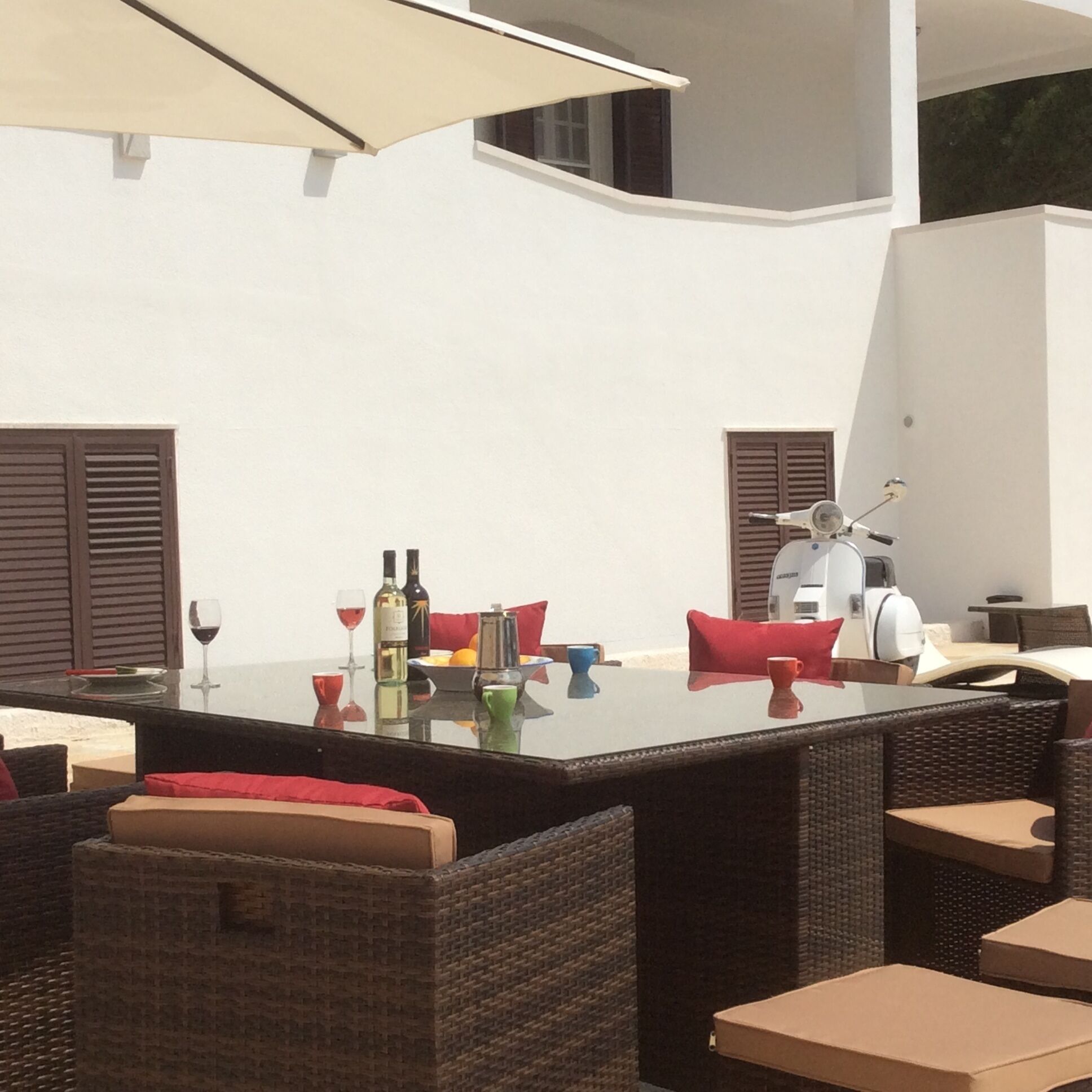 Een terras met rieten meubels, een tafel gedekt met wijnglazen, flessen en een koffiepot.