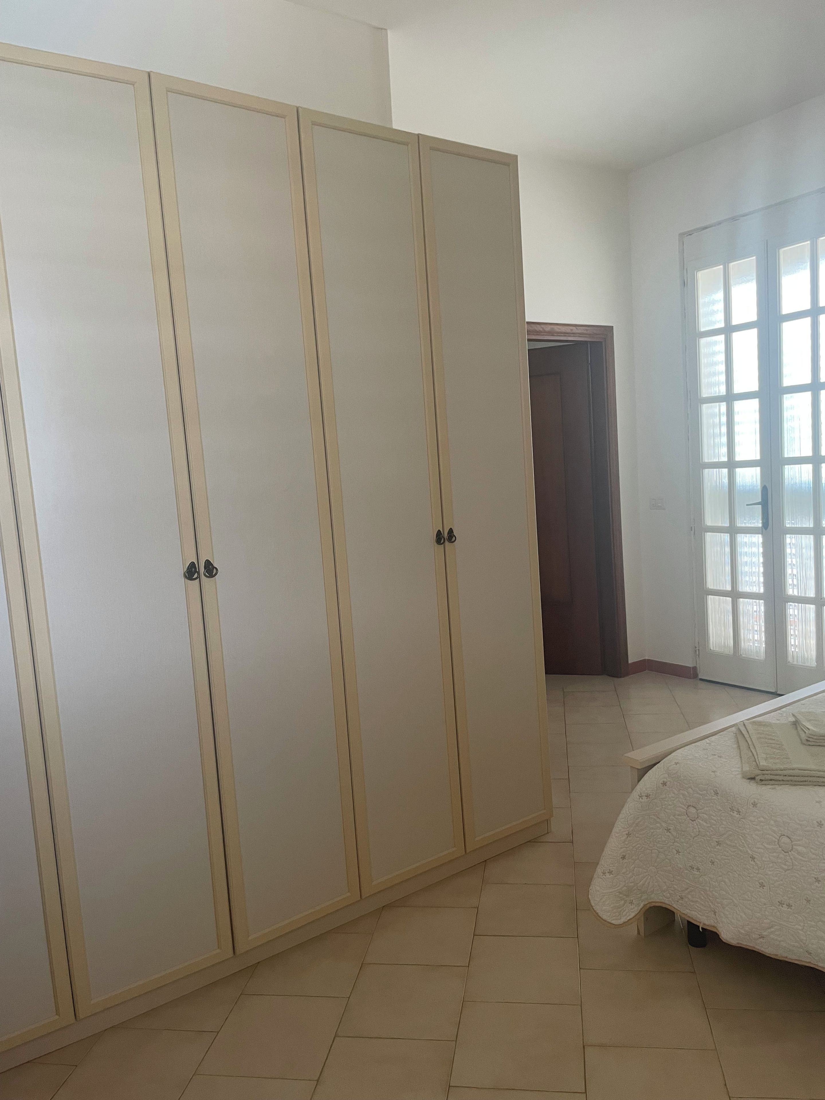 A bedroom with a large wardrobe, a bed with a floral bedspread, and a window with blinds.