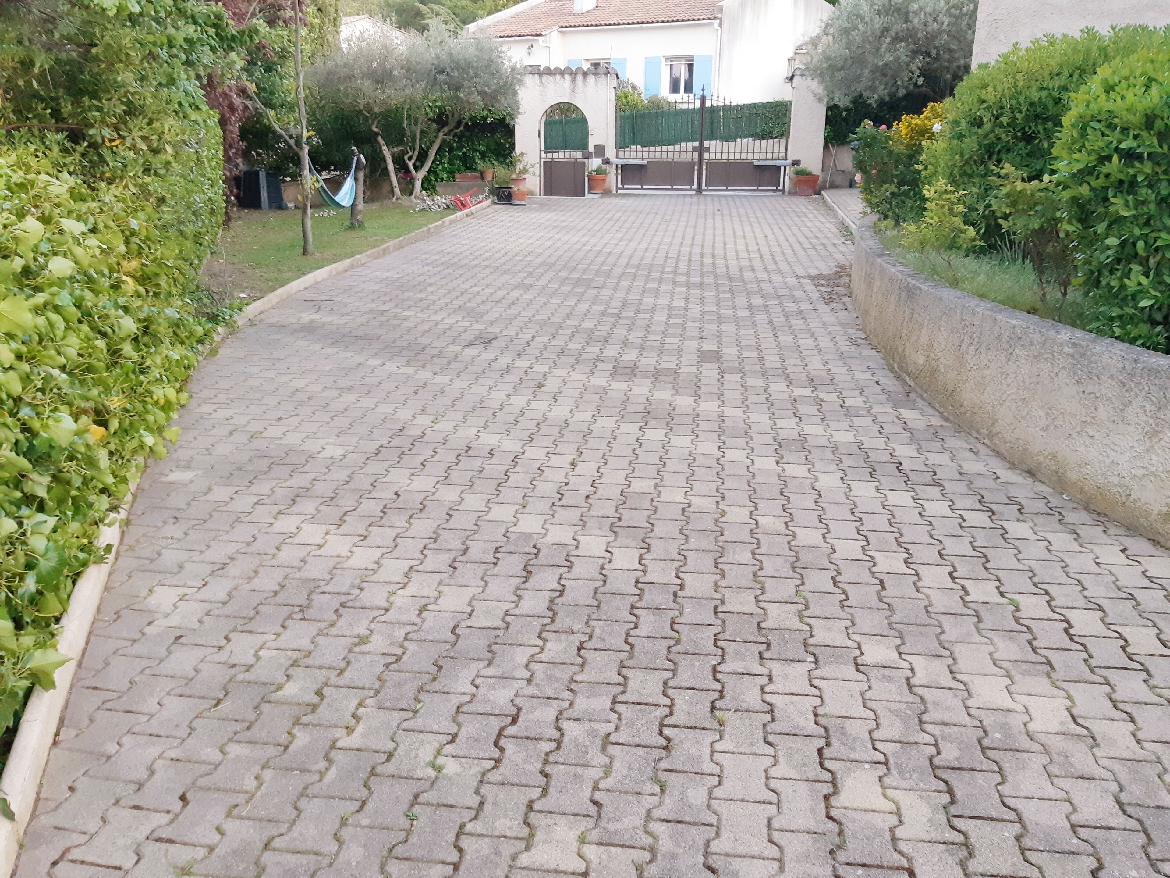 A paved pathway leading to a gated entrance with a house in the background.