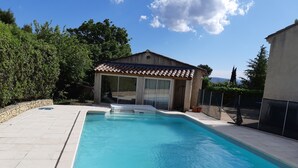 Una piscina con un borde de baldosas, una zona de estar cubierta y una pared de piedra.