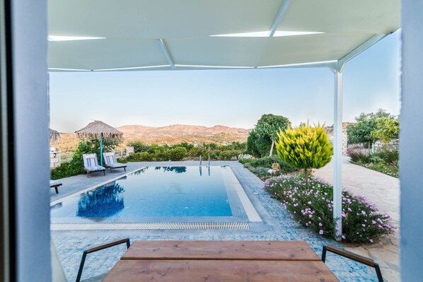 An infinity pool with a clear view of mountains, surrounded by lounge chairs and a covered patio area.