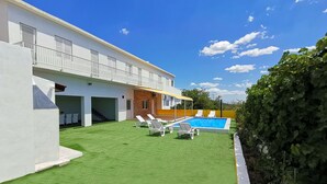 Ett modernt hus med en swimmingpool, en täckt uteplats och en välskött gräsmatta.