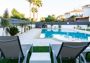 Une piscine avec deux chaises longues placées en face, entourée d’un petit muret et de palmiers.