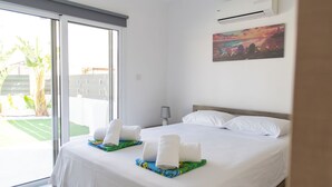 Une chambre d’hôtel avec un grand lit, une porte-fenêtre coulissante donnant sur un balcon, un appareil de climatisation et un tableau au mur.